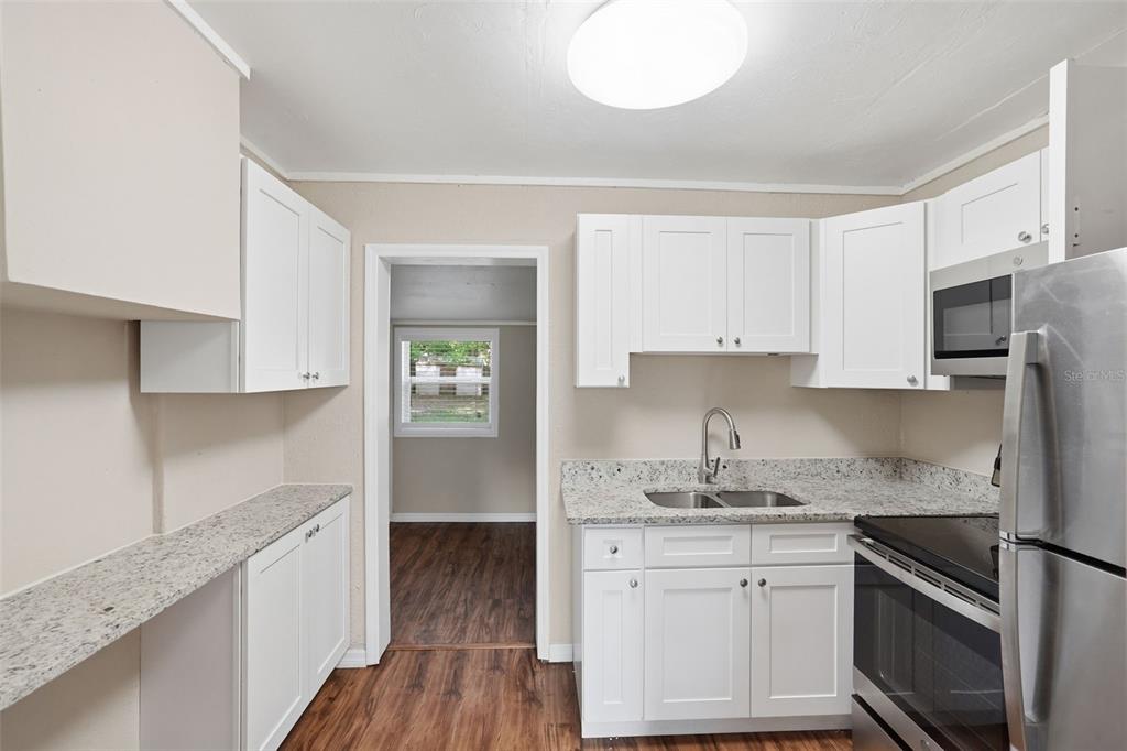 A kitchen features white cabinets, granite countertops, stainless steel appliances, and wood-look flooring — 303 JOSEPHINE AVENUE, FRUITLAND PARK, FL