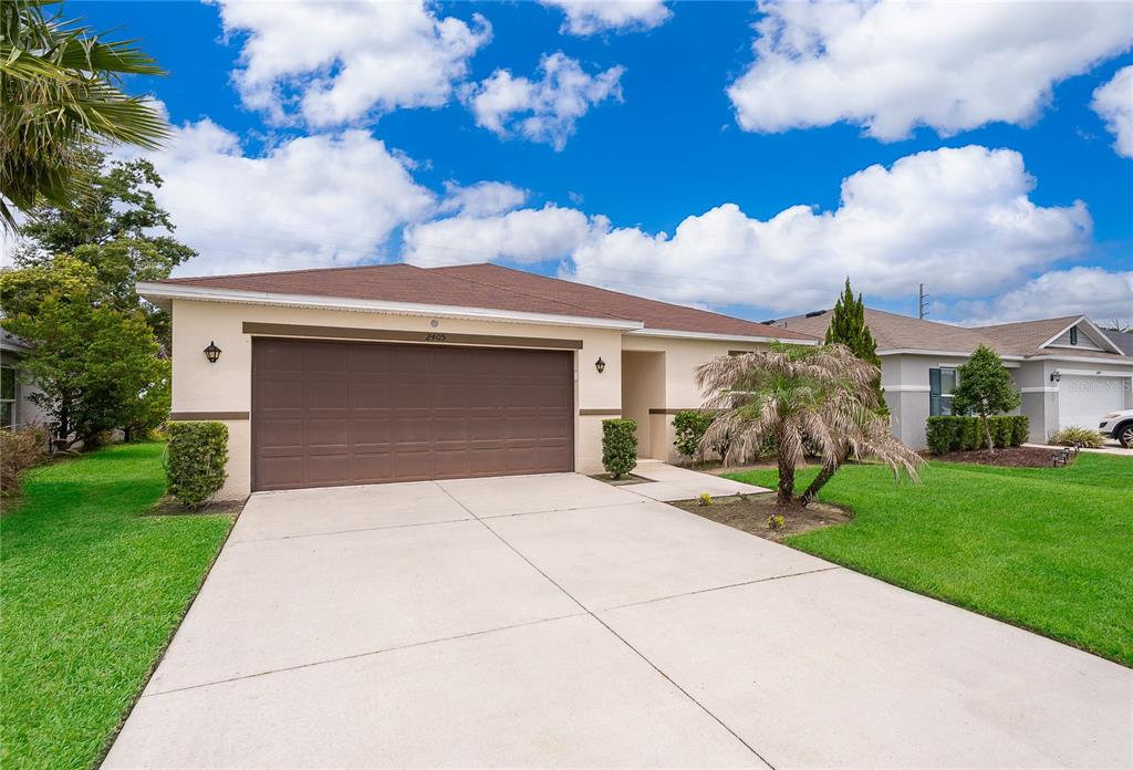 A single-story house with a brown garage door, concrete driveway, and a small palm tree — 2405 BULRUSH DRIVE, ST CLOUD, FL