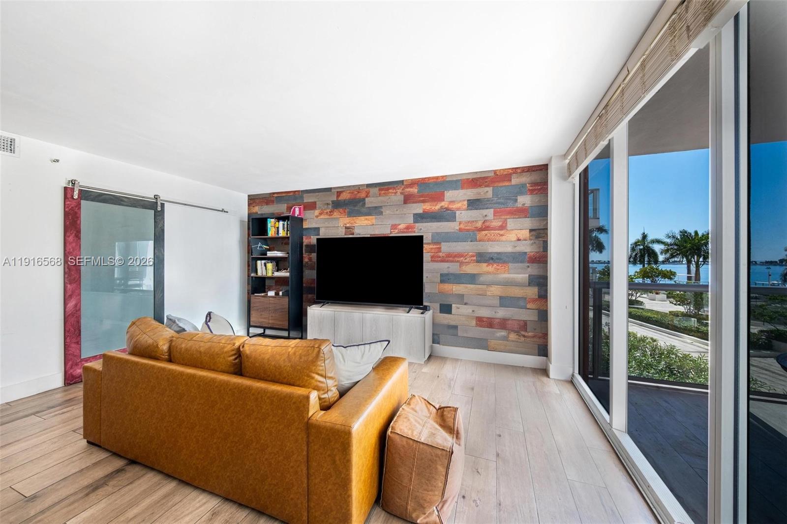A living room features a leather sofa, a wood-plank accent wall, and a balcony view — 1541 Brickell Ave # C406, Miami FL 33129, MIAMI, FL