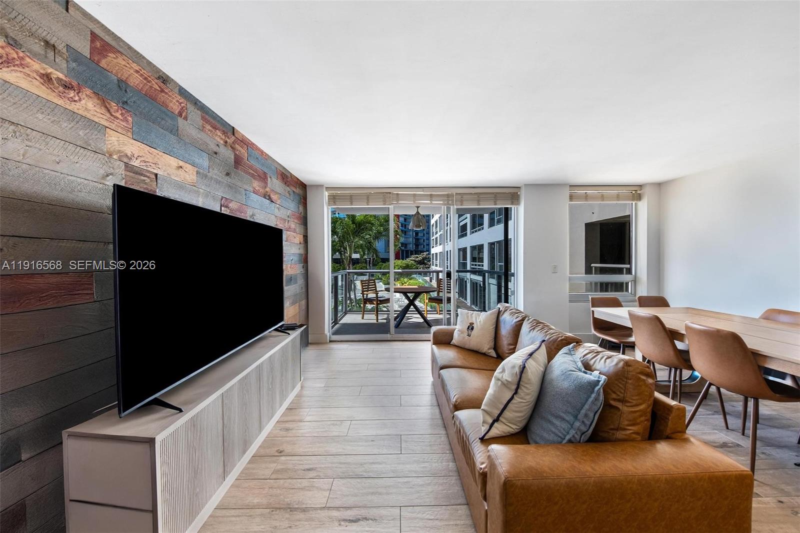 A living room features a wood-paneled accent wall, a leather sofa, and a balcony view — 1541 Brickell Ave # C406, Miami FL 33129, MIAMI, FL