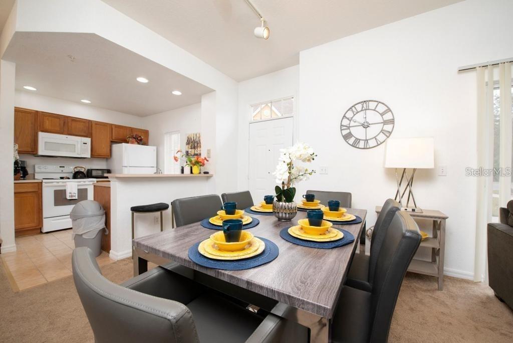 A dining room with a gray table, yellow place settings, and an adjacent open kitchen — 4012 SANTA MARIA DRIVE UNIT 101, KISSIMMEE, FL