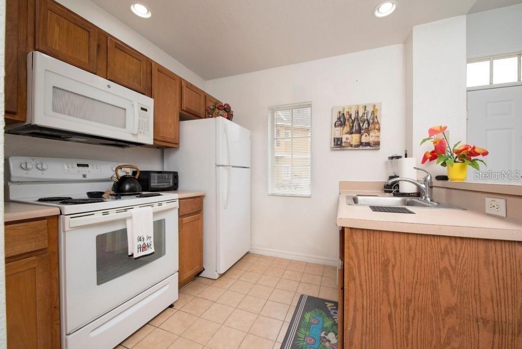 A kitchen with white appliances, wooden cabinets, beige countertops, and tile flooring — 4012 SANTA MARIA DRIVE UNIT 101, KISSIMMEE, FL