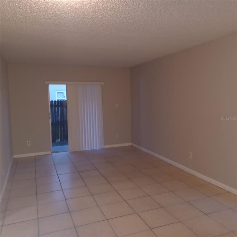 An empty room with beige tile flooring, light-colored walls, and a sliding glass door — 1508 E 127TH AVENUE UNIT B, TAMPA, FL