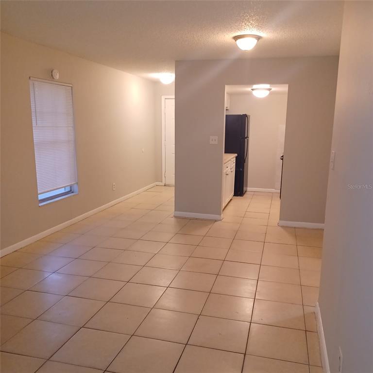 A tiled living area leads into a kitchen with white cabinets and a black refrigerator — 1508 E 127TH AVENUE UNIT B, TAMPA, FL
