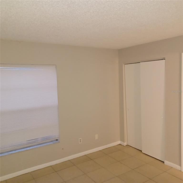 A bedroom with light-colored walls, tile flooring, a window with blinds, and a sliding closet — 1508 E 127TH AVENUE UNIT B, TAMPA, FL