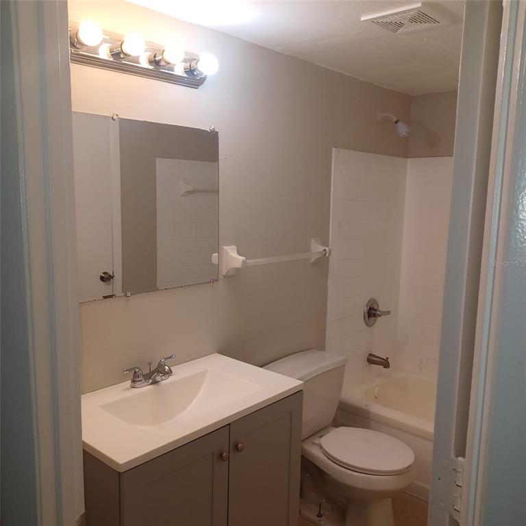 A bathroom features a gray vanity, a wall-mounted mirror, a toilet, and a shower-tub combo — 1508 E 127TH AVENUE UNIT B, TAMPA, FL