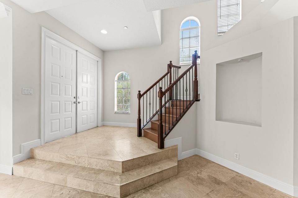 An entryway features a raised tiled landing, a double front door, and a wooden staircase — 210 NE 69th Circle, Boca Raton FL 33487, BOCA RATON, FL