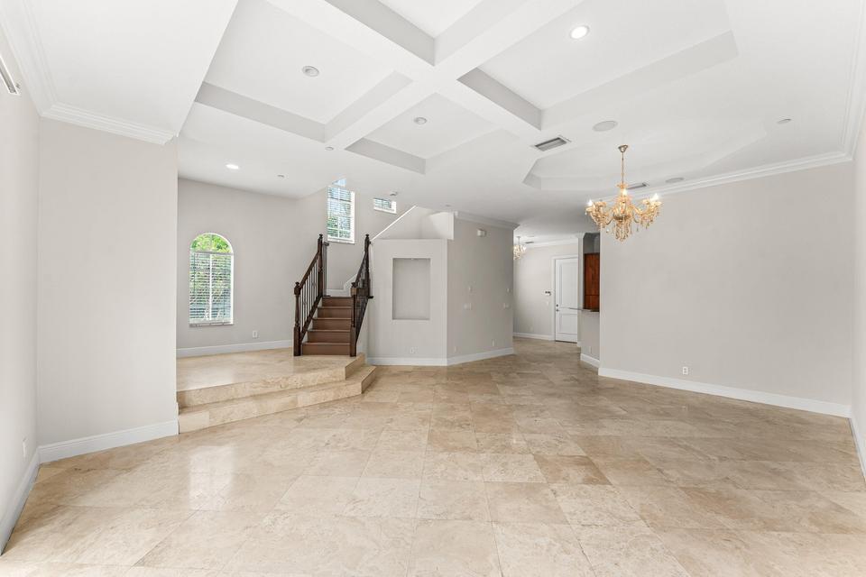 A spacious room with a coffered ceiling, stone tile flooring, and a wooden staircase — 210 NE 69th Circle, Boca Raton FL 33487, BOCA RATON, FL