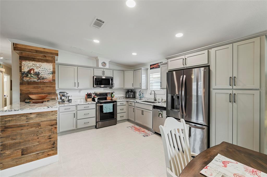 A kitchen features light gray cabinets, stainless steel appliances, and a rustic wood-paneled accent wall — 24500 RIO VILLA LAKES CIRCLE, PUNTA GORDA, FL