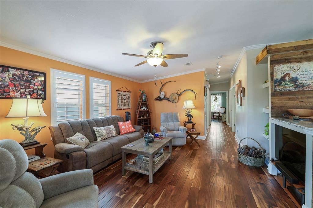 A living room features orange walls, wood flooring, a ceiling fan, and a fireplace — 24500 RIO VILLA LAKES CIRCLE, PUNTA GORDA, FL