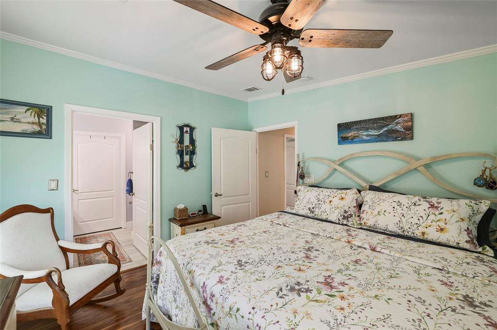 A bedroom features light green walls, a floral bedspread, a ceiling fan, and a rocking chair — 24500 RIO VILLA LAKES CIRCLE, PUNTA GORDA, FL