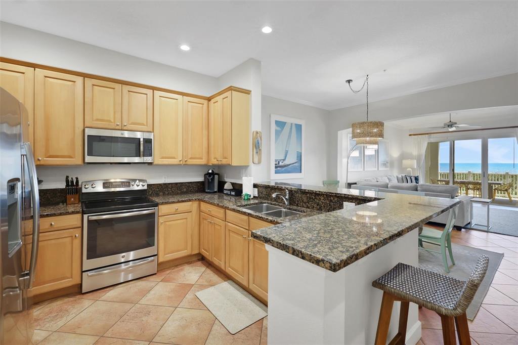 A kitchen with light wood cabinets, granite countertops, and a breakfast bar overlooking the ocean — 900 CINNAMON BEACH WAY UNIT 822, PALM COAST, FL