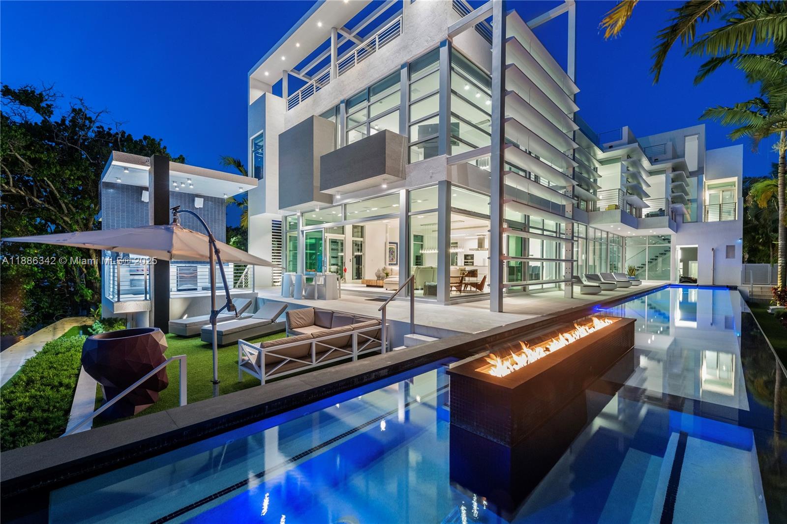 A modern multi-story house features a swimming pool with a central fire feature at dusk — 440 S Hibiscus Dr, Miami Beach FL 33139, MIAMI BEACH, FL