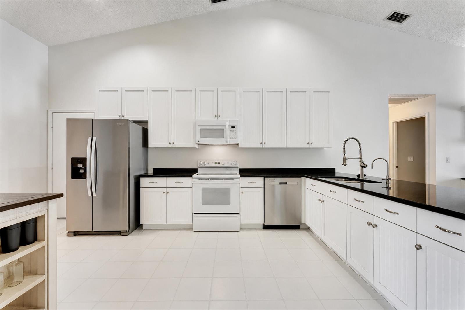 A kitchen features white cabinetry, black countertops, stainless steel appliances, and white tile flooring — 7312 Heathley Drive, Lake Worth FL 33467, LAKE WORTH, FL