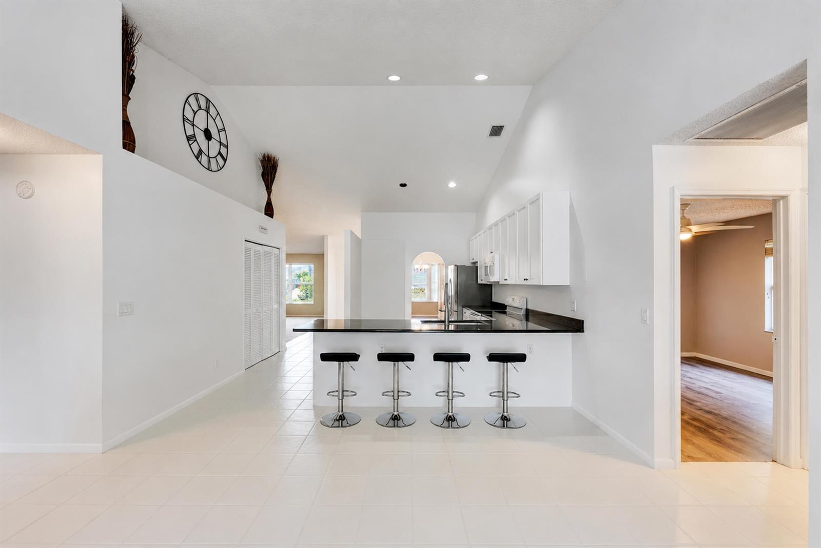 A kitchen with white cabinets, black countertops, and four bar stools on a tiled floor — 7312 Heathley Drive, Lake Worth FL 33467, LAKE WORTH, FL