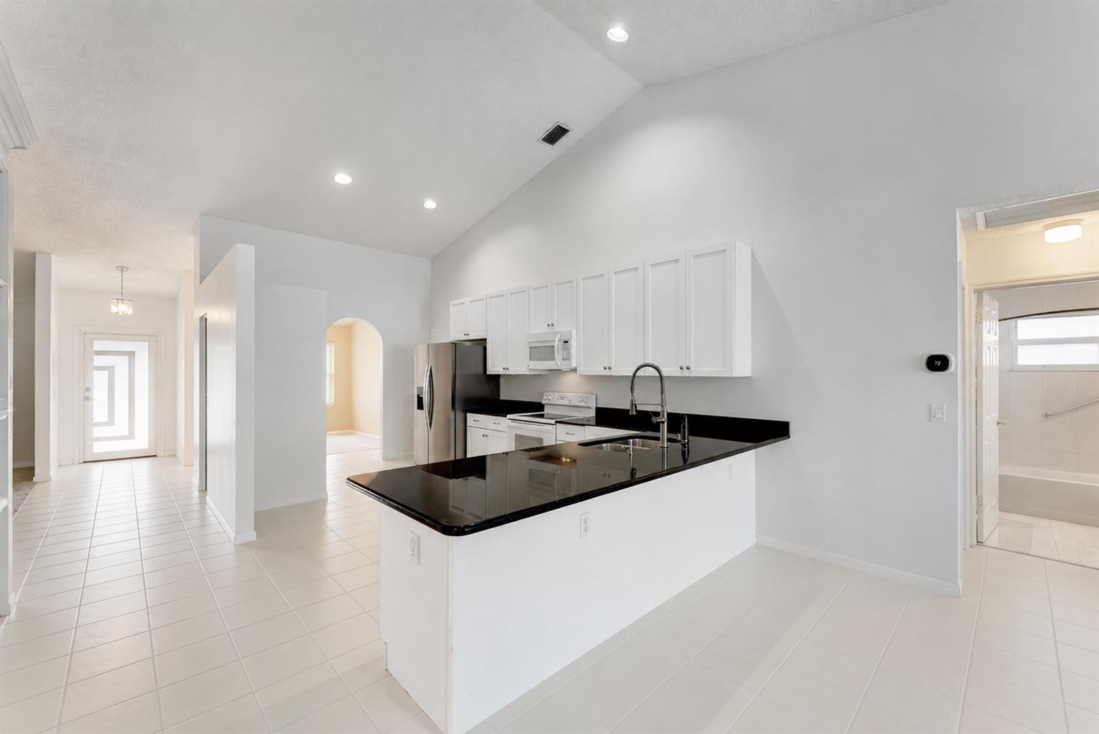 A kitchen with white cabinets, black countertops, and tile flooring under a vaulted ceiling — 7312 Heathley Drive, Lake Worth FL 33467, LAKE WORTH, FL
