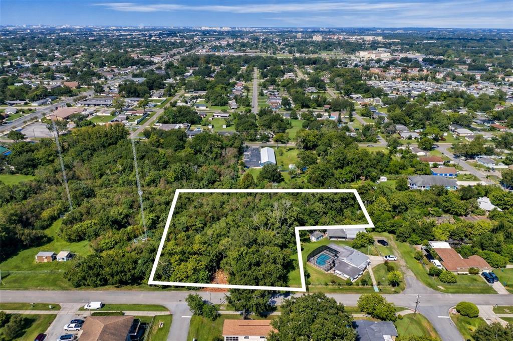 An aerial view shows a wooded, L-shaped vacant lot outlined in white near residential houses — 110 PRINCE STREET, ORLANDO, FL