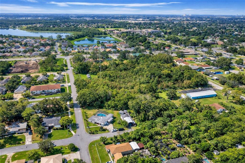 An aerial view shows a suburban neighborhood with houses, dense trees, and a nearby lake — 110 PRINCE STREET, ORLANDO, FL