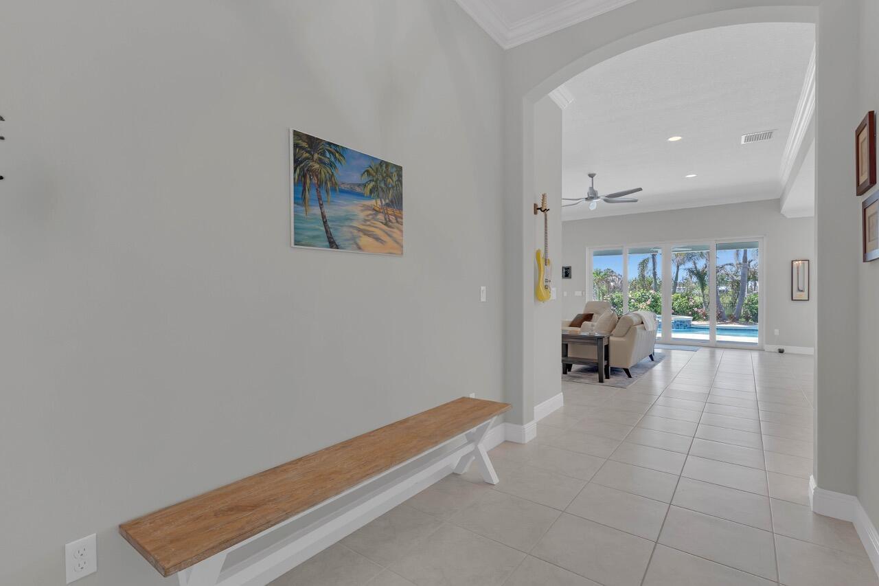 A hallway with a wooden bench and wall art leads to a living room with pool views — 7203 33rd Square, Vero Beach FL 32967, VERO BEACH, FL