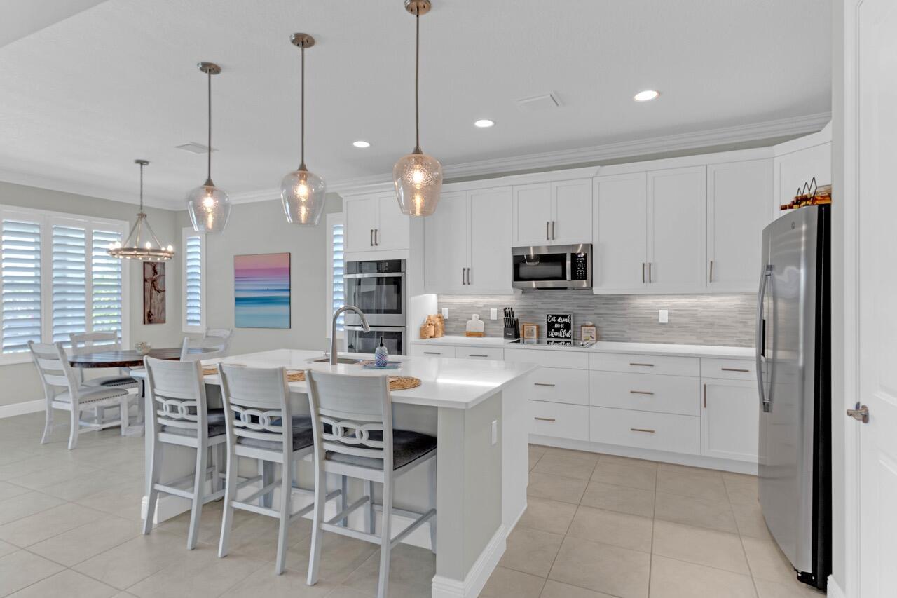 A modern kitchen features white cabinetry, a central island with bar seating, and stainless appliances — 7203 33rd Square, Vero Beach FL 32967, VERO BEACH, FL