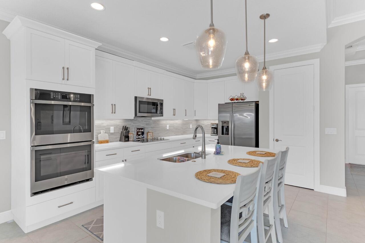 A modern kitchen features white cabinetry, stainless steel appliances, a large island, and pendant lighting — 7203 33rd Square, Vero Beach FL 32967, VERO BEACH, FL