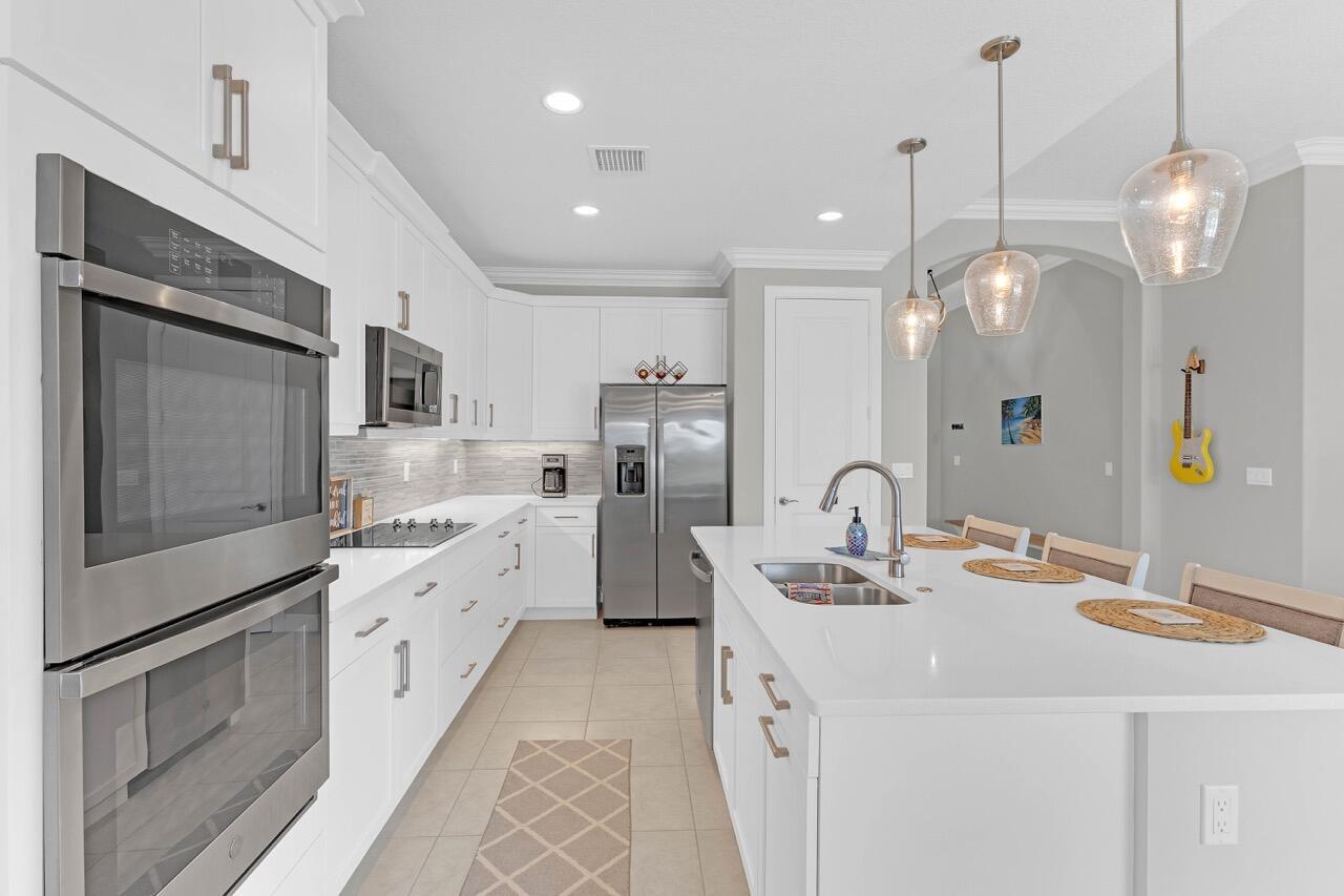 A modern kitchen features white cabinetry, stainless steel appliances, a large island, and pendant lighting — 7203 33rd Square, Vero Beach FL 32967, VERO BEACH, FL