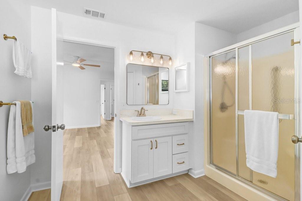 A bathroom features a white vanity, a glass-enclosed shower, and light wood-look flooring — 4949 PLEASANT HOLLOW TRAIL UNIT 211, LAKELAND, FL