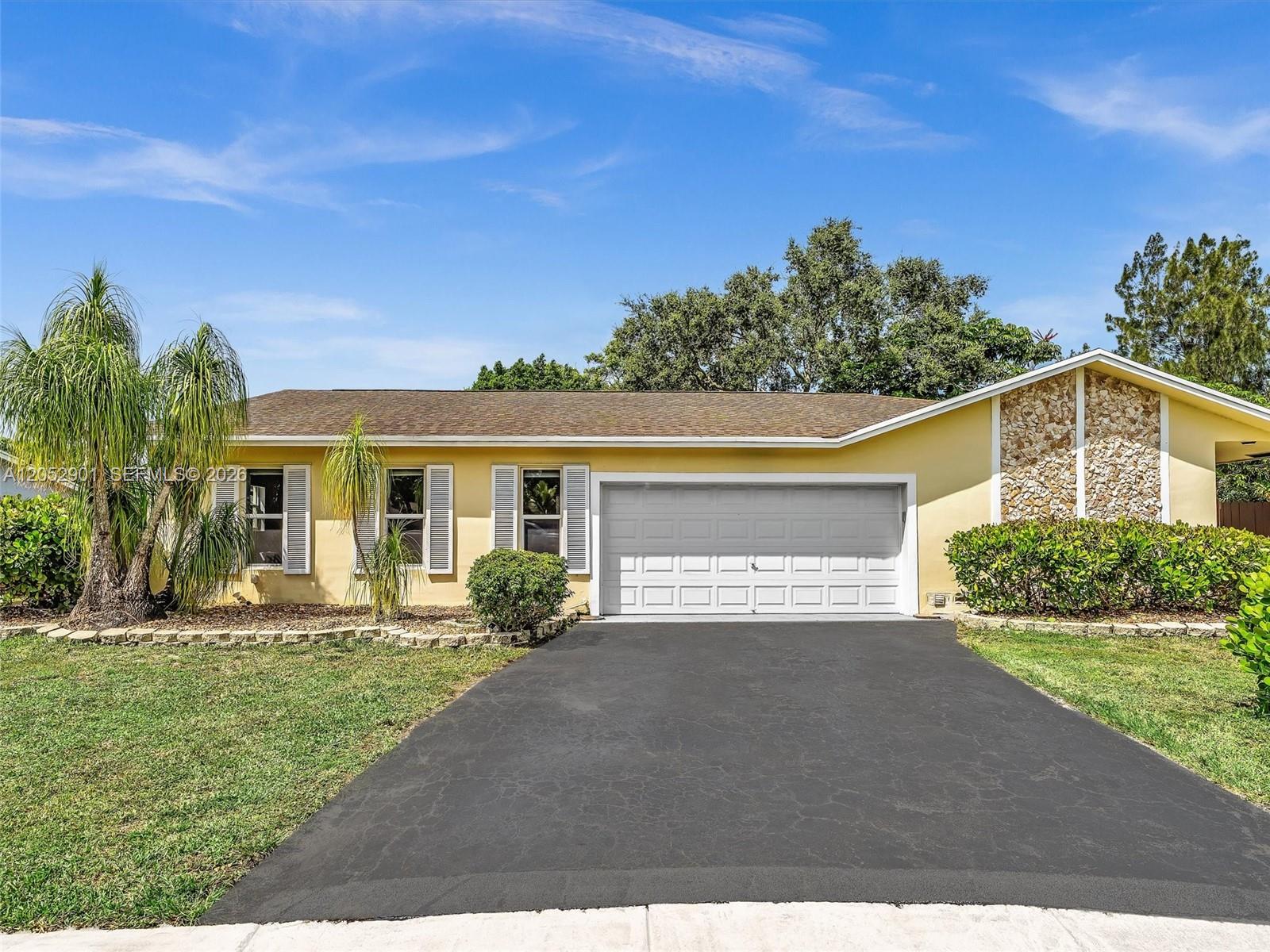 A single-story yellow house with a stone accent wall, a two-car garage, and palm trees — 8754 SW 50th Pl, Cooper City FL 33328, COOPER CITY, FL