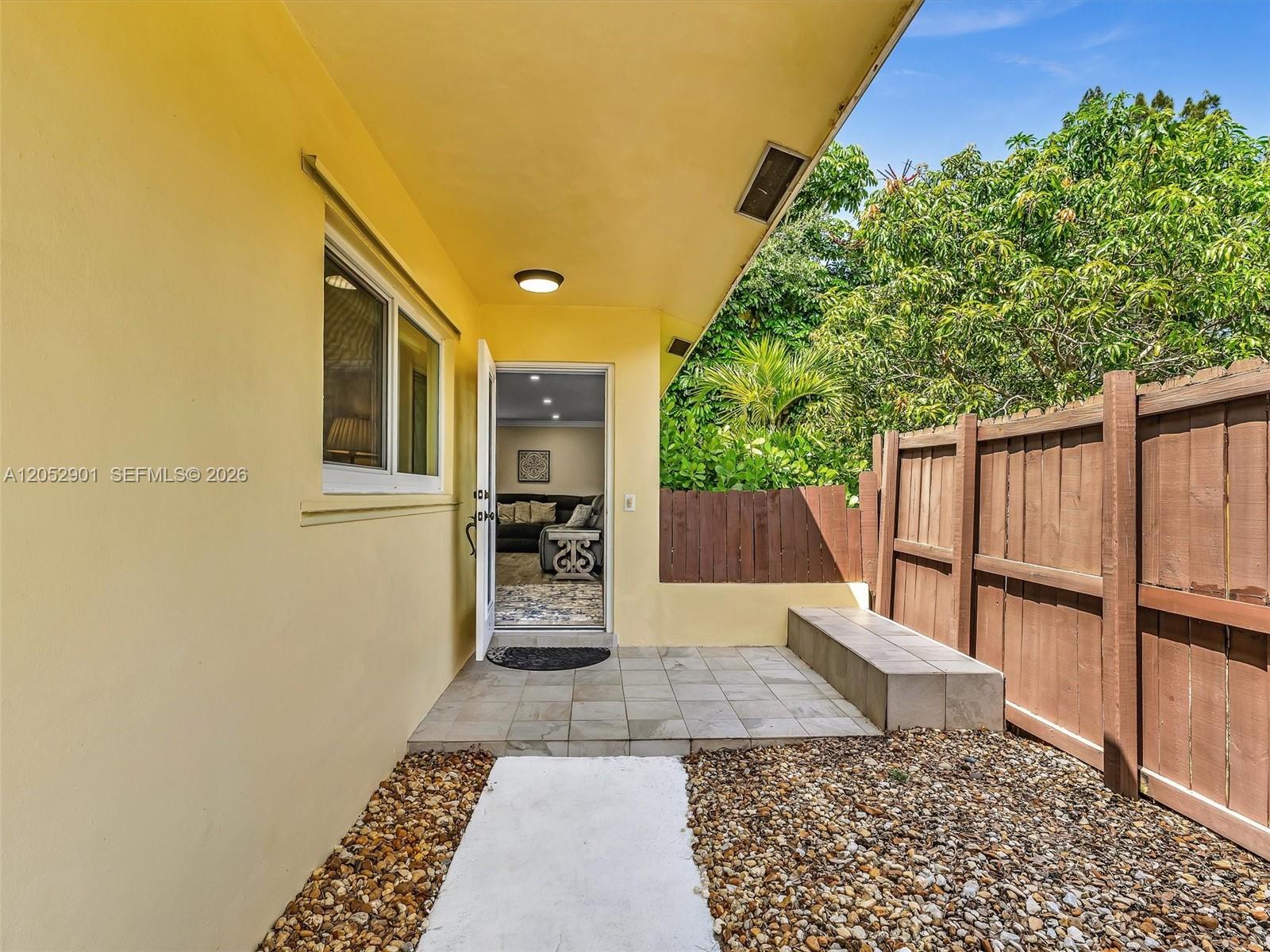 A yellow exterior wall leads to an open door revealing a furnished living room — 8754 SW 50th Pl, Cooper City FL 33328, COOPER CITY, FL
