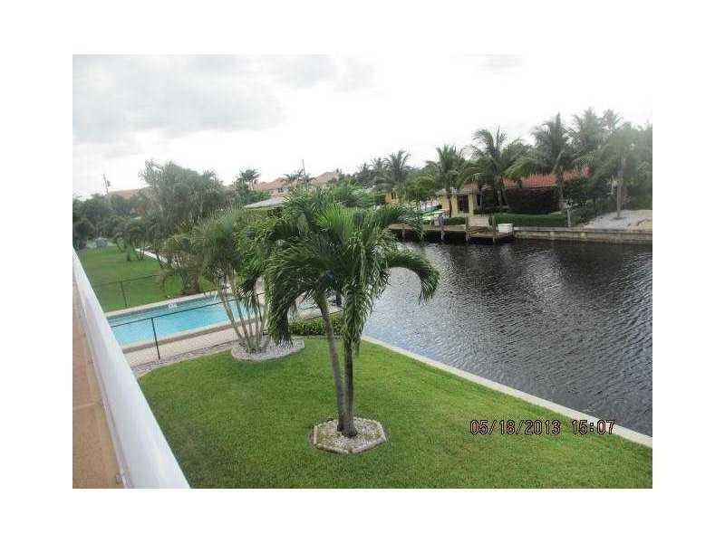 A view of a backyard lawn, a swimming pool, and a canal with palm trees — 301 E Mcnab Road E # 106, Pompano Beach FL 33060, POMPANO BEACH, FL