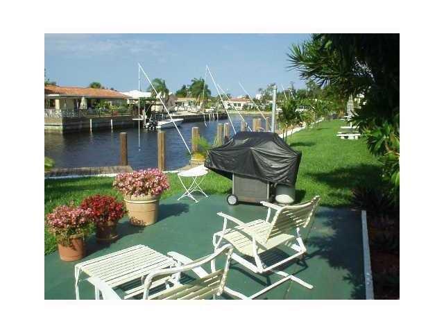 A patio with outdoor furniture and a covered grill overlooks a canal with a boat — 301 E Mcnab Road E # 106, Pompano Beach FL 33060, POMPANO BEACH, FL