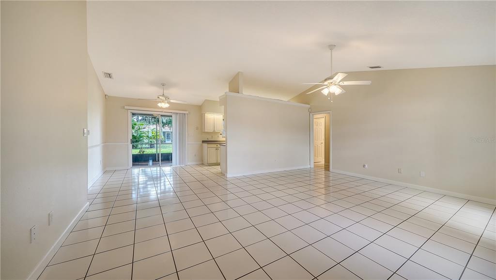 An open-concept living area features white tile flooring, vaulted ceilings, and a sliding glass door — 3826 BEEBER STREET, NORTH PORT, FL