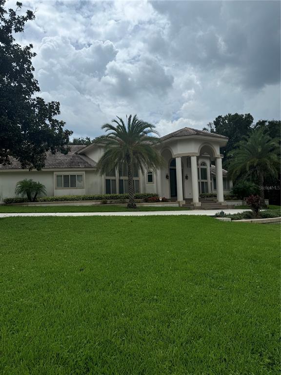 A single-story house with a columned entryway and palm trees sits behind a large lawn — 1040 SWEETWATER CLUB BOULEVARD, LONGWOOD, FL