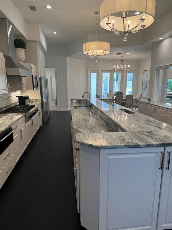 A kitchen features white cabinets, granite countertops, a large island, and dark flooring — 1040 SWEETWATER CLUB BOULEVARD, LONGWOOD, FL