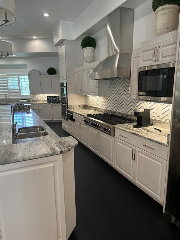 A modern kitchen features white cabinetry, granite countertops, a chevron backsplash, and dark flooring — 1040 SWEETWATER CLUB BOULEVARD, LONGWOOD, FL