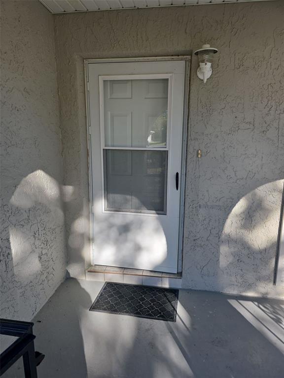 A white storm door with a glass panel is centered on a textured exterior wall — 7251 MCGINNES COURT, WEEKI WACHEE, FL