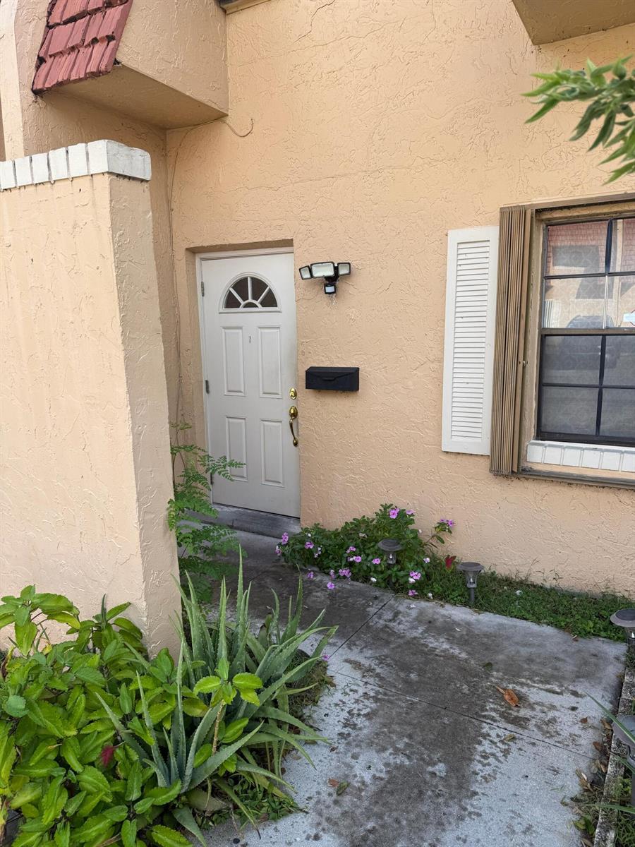 A beige exterior wall features a white front door, a black mailbox, and a light — 76 Ann Lee Lane, Tamarac FL 33319, TAMARAC, FL