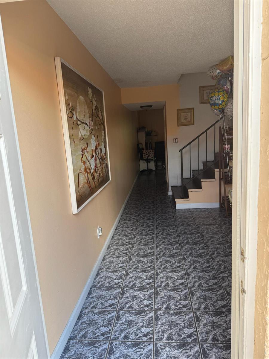 A hallway with gray marble-patterned tile flooring leads to a staircase and a back room — 76 Ann Lee Lane, Tamarac FL 33319, TAMARAC, FL