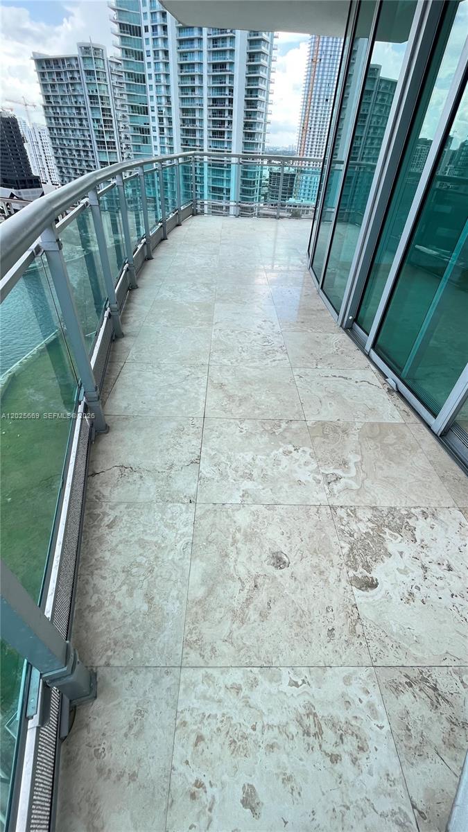 A balcony with light-colored stone tile flooring overlooks a city skyline and water — 350 S Miami Ave # 2302, Miami FL 33130, MIAMI, FL