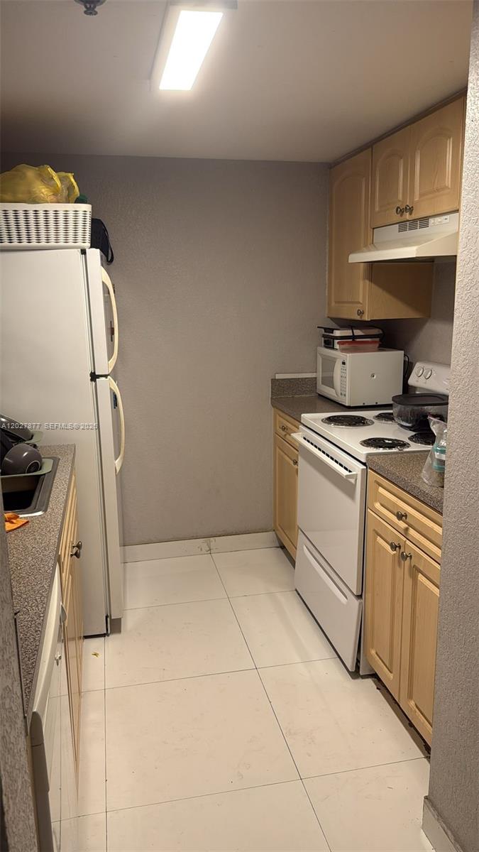 A narrow kitchen features light wood cabinets, white appliances, and white tile flooring — 814 NW 36th Ave # 208, Miami FL 33125, MIAMI, FL