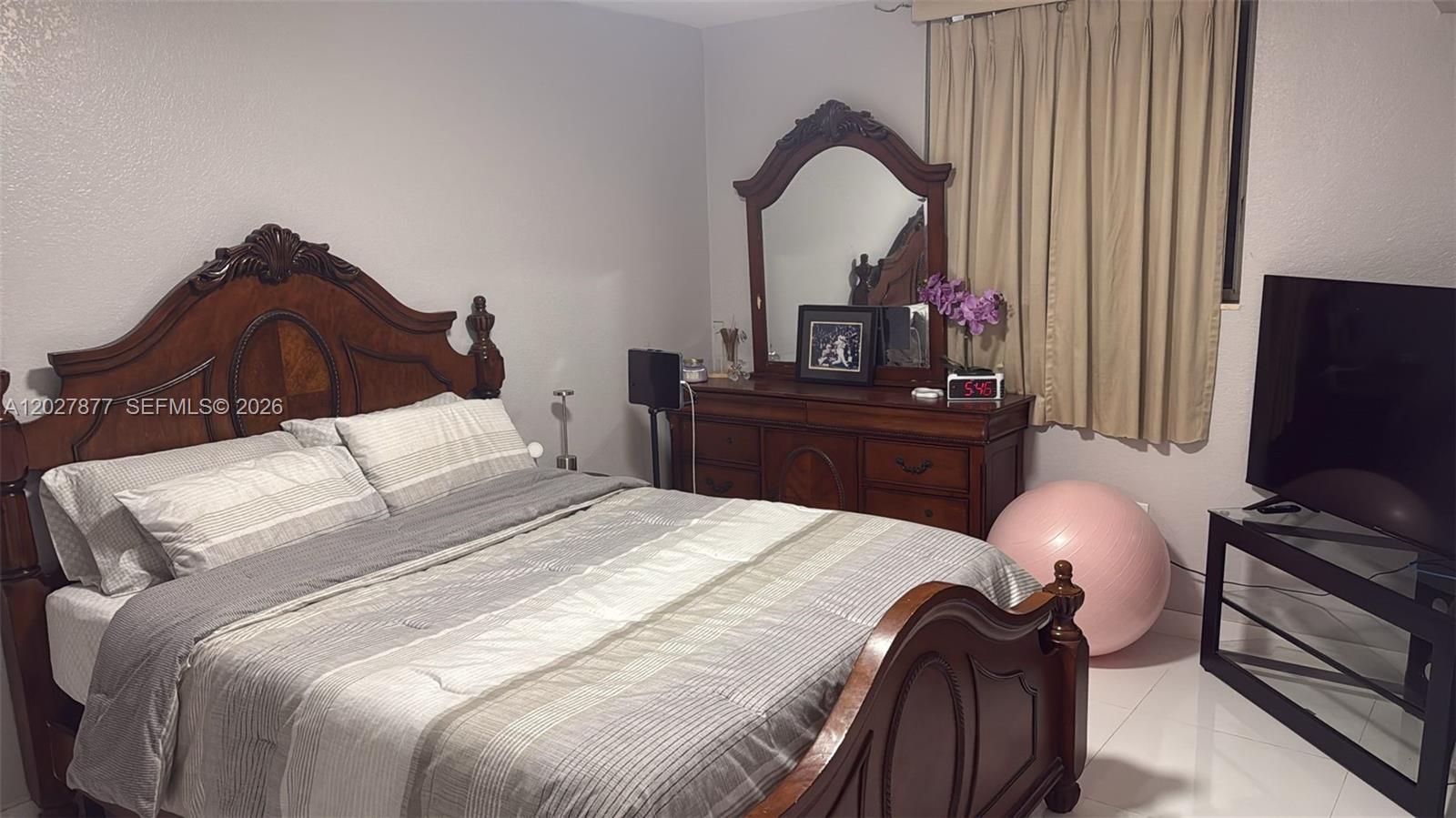 A bedroom features a wooden bed frame, a matching dresser with a mirror, and a television — 814 NW 36th Ave # 208, Miami FL 33125, MIAMI, FL