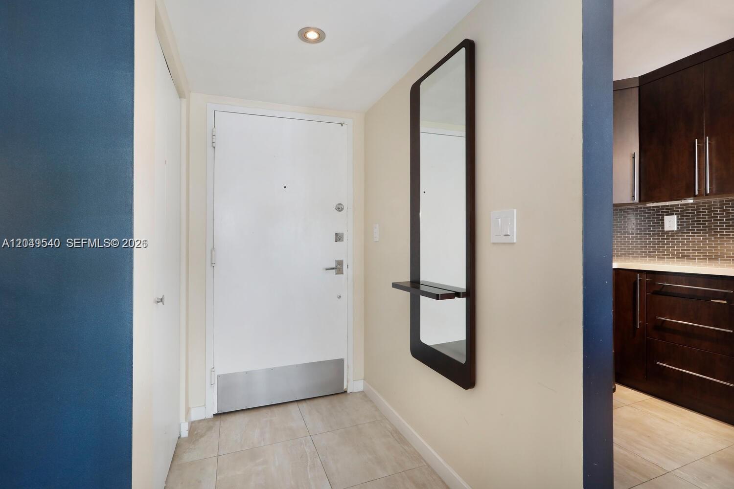 An entryway features a white door, a wall-mounted mirror with a shelf, and tile flooring — 145 SE 25th Rd # 502, Miami FL 33129, MIAMI, FL