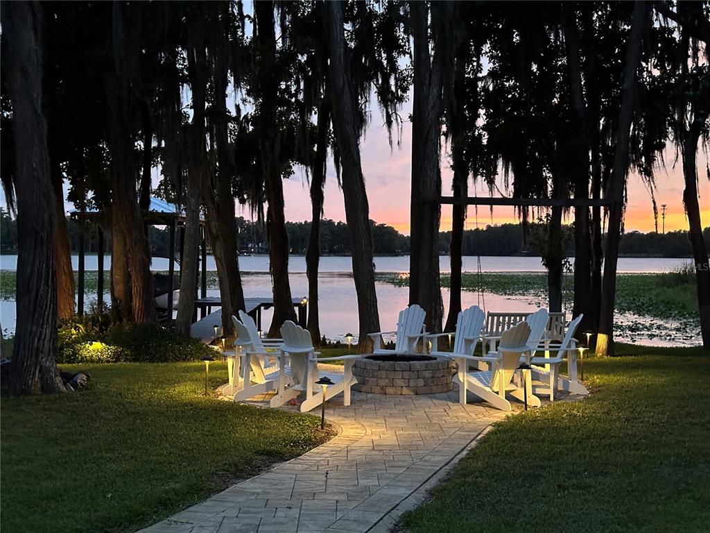 A stone fire pit with white Adirondack chairs sits on a patio overlooking a lake — 5035 CONNER DRIVE, LAND O LAKES, FL