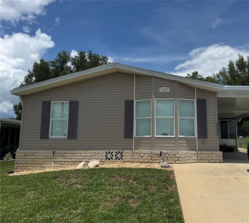 The exterior of a single-story house features tan siding, a brick foundation, and a driveway — 37437 GILL AVENUE, ZEPHYRHILLS, FL