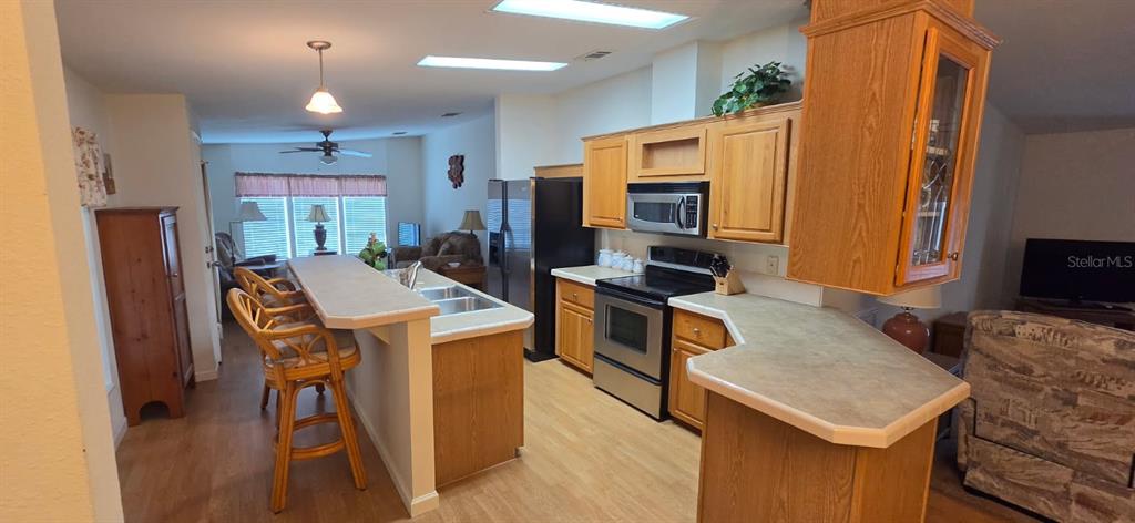 A kitchen with light wood cabinets, stainless steel appliances, and a breakfast bar with stools — 37437 GILL AVENUE, ZEPHYRHILLS, FL