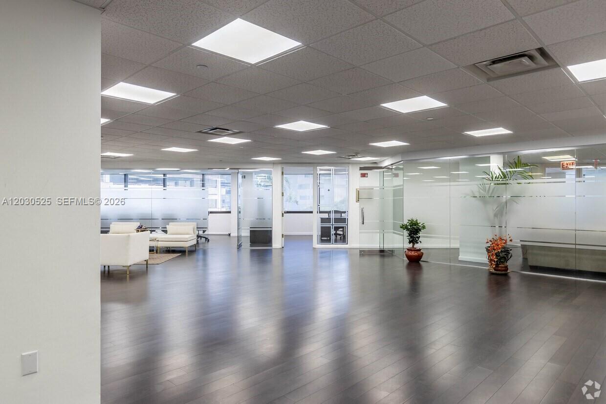 A modern office interior features dark wood flooring, glass-walled partitions, and recessed ceiling lighting — FORT LAUDERDALE, FL