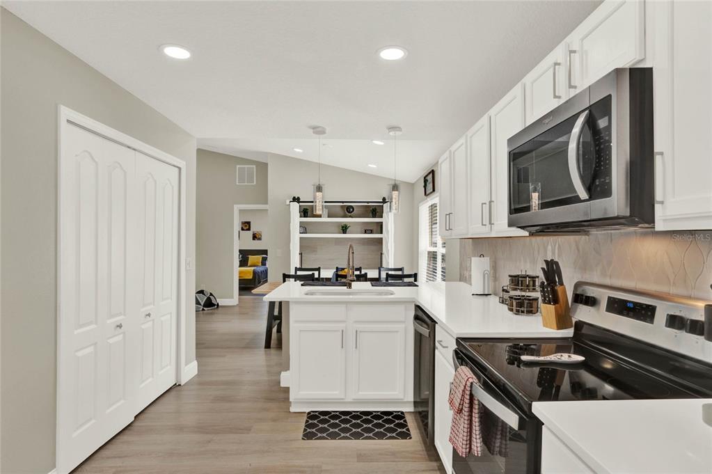 A white kitchen features a center island, stainless steel appliances, and light wood-look flooring — 188 RIDGEMONT COURT, DAVENPORT, FL