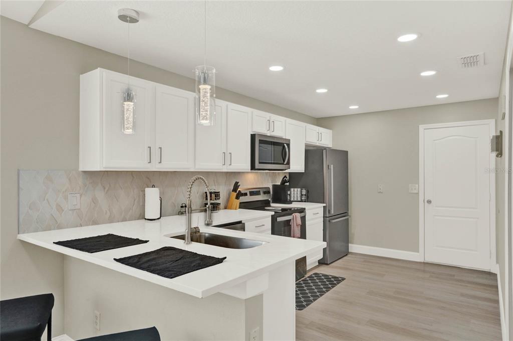 A modern kitchen features white cabinets, stainless steel appliances, quartz countertops, and light wood flooring — 188 RIDGEMONT COURT, DAVENPORT, FL