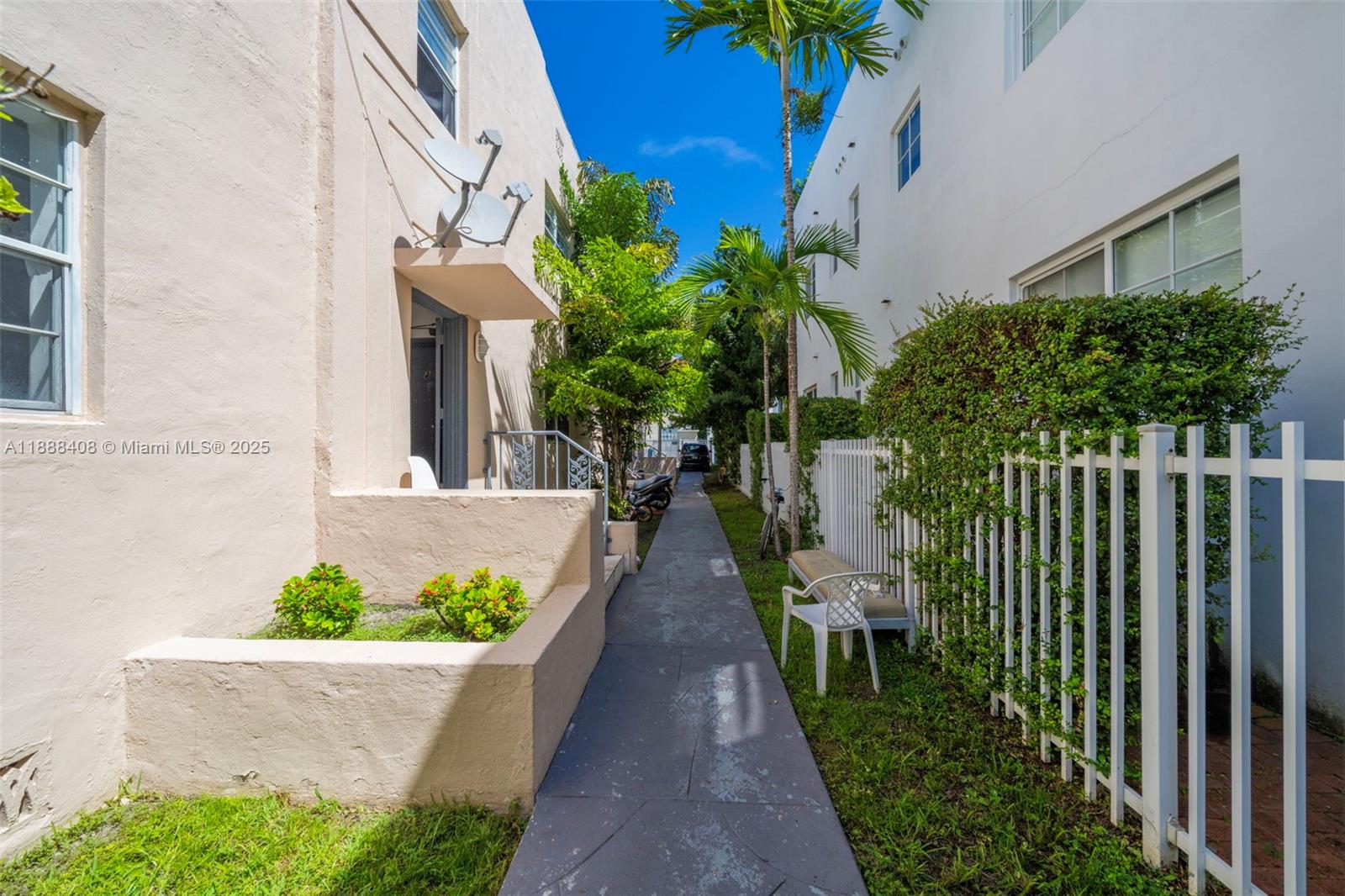 A narrow concrete walkway runs between two multi-story buildings with landscaping and a white fence — 1329 Pennsylvania Ave, Miami Beach FL 33139, MIAMI BEACH, FL