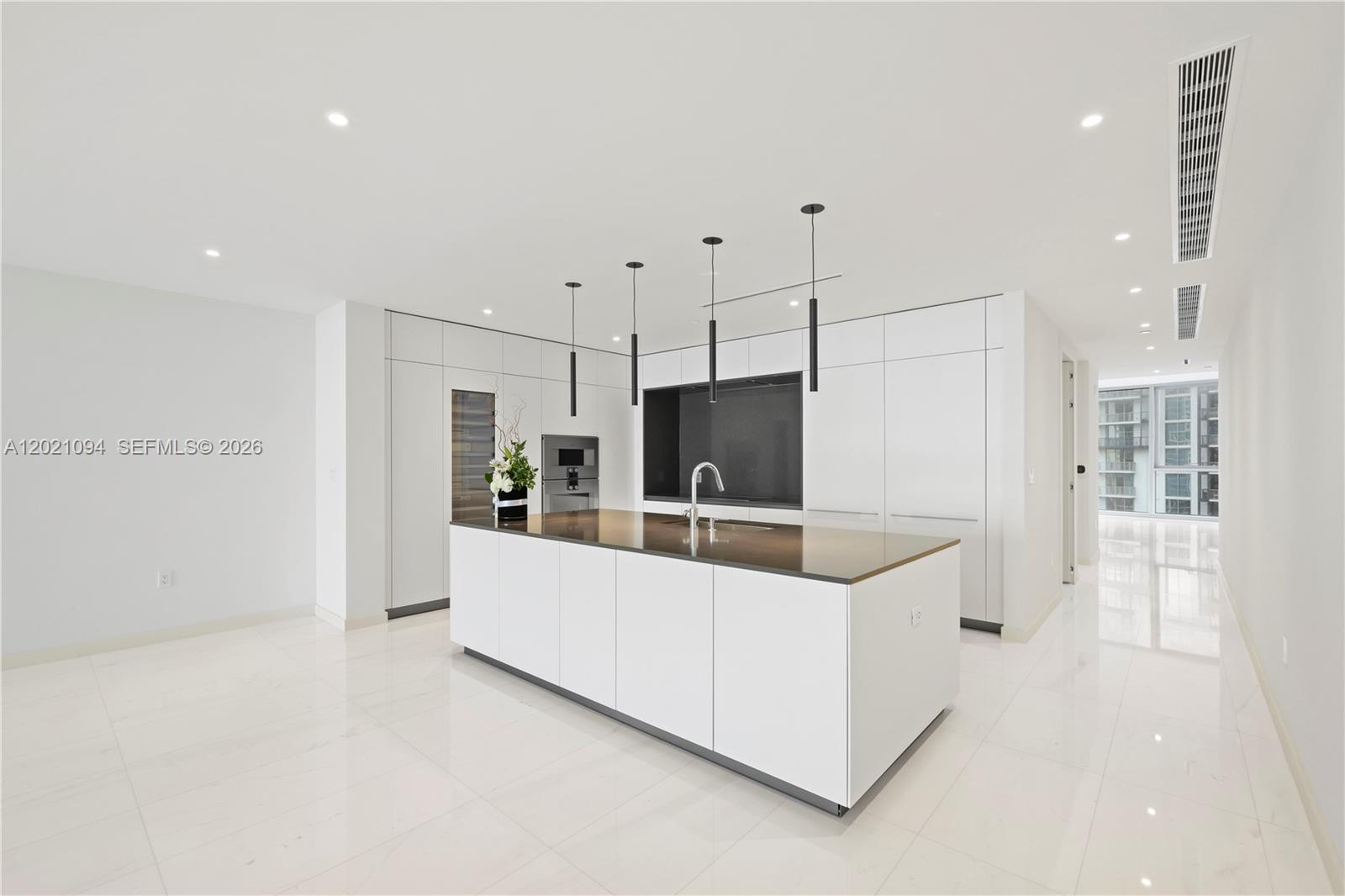 A modern kitchen features a white island, dark countertops, and minimalist cabinetry — 300 Biscayne Blvd Way # 3404C, Miami FL 33131, MIAMI, FL